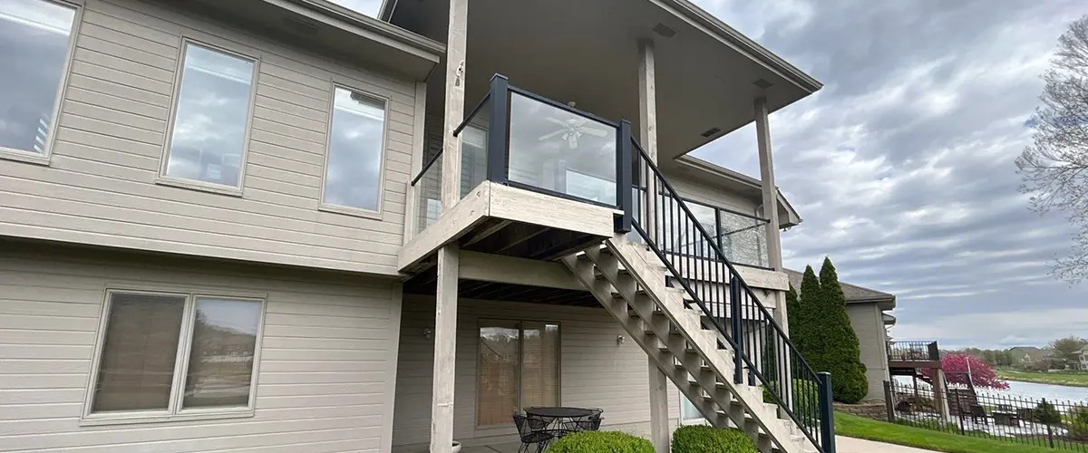 Deck Repair in Avoca, IA Backyard view of raised deck with modern railing and staircase, landscaped with shrubs and decorative rock edging - on page image
