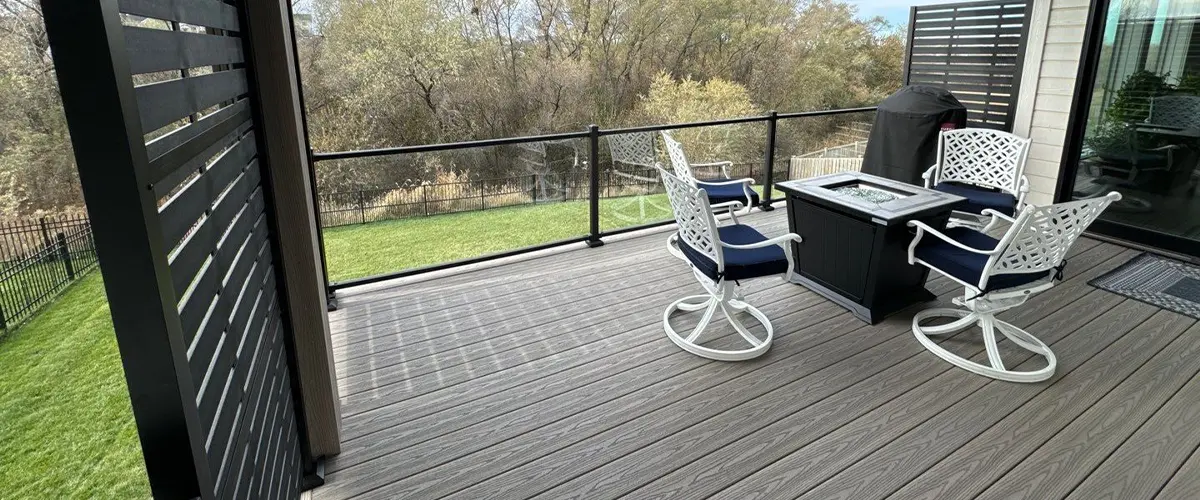 Deck Repair in Underwood, IA Covered composite deck with privacy panels, black railing, and outdoor seating set overlooking green backyard and trees.