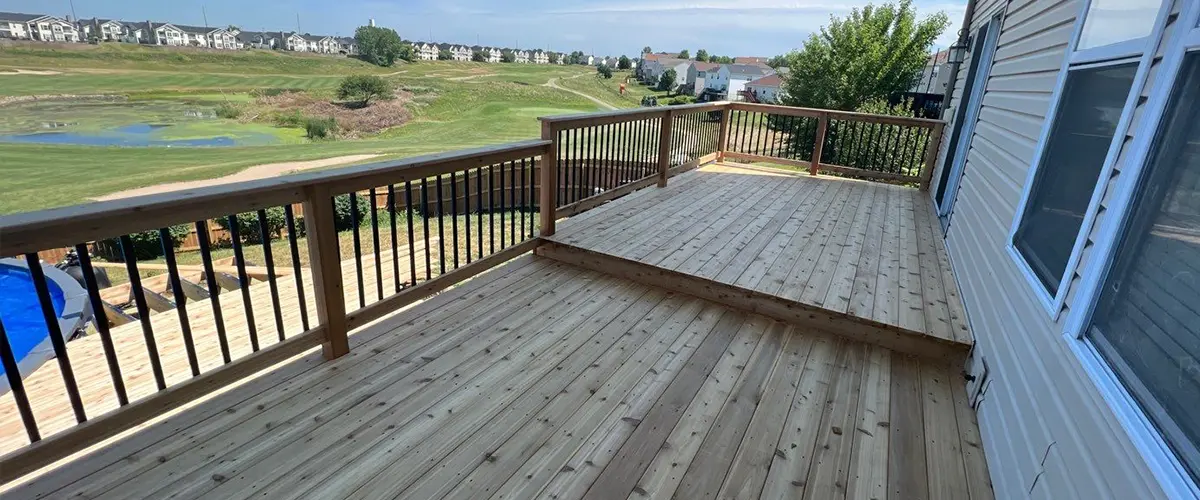 Deck Repair in Avoca, IA Newly built raised wood deck with black railing overlooking a golf course and suburban neighborhood under blue skies