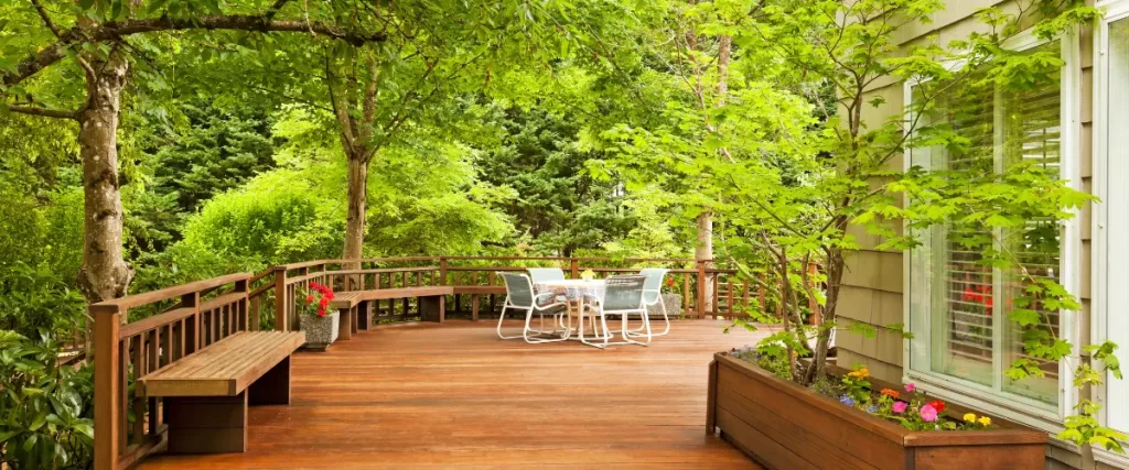 Wooden deck with a white outdoor dining set in a lush, green garden.