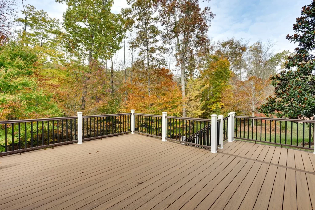 A completed wooden deck with white and black railings, overlooking a wooded area with autumn foliage.