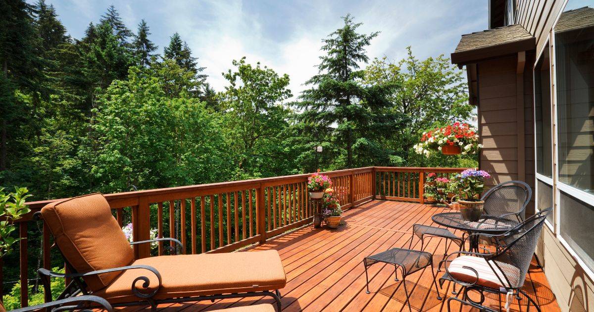 Blog Stained wooden deck with lounge chairs and potted plants, surrounded by trees.