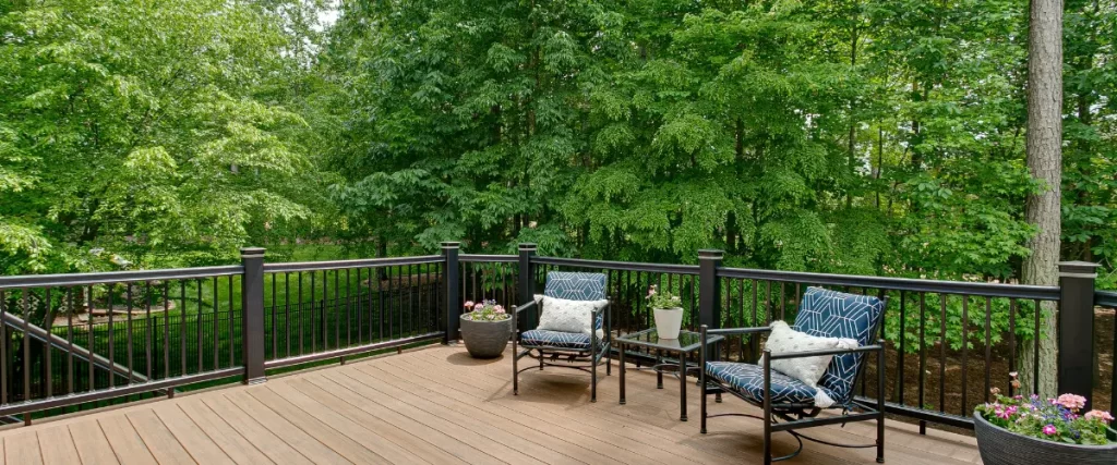 How Omaha’s High Humidity Affects Wooden Decks & the Best Ways to Prevent Rot A cozy wooden deck with cushioned seating and a black railing, set against a lush green forest.