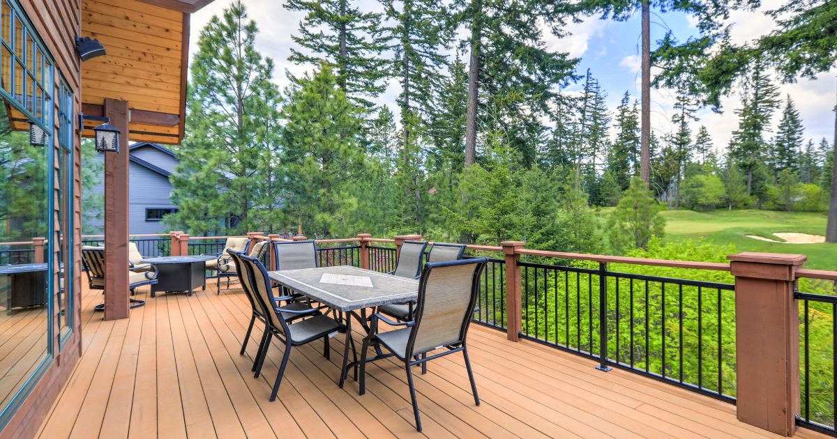 Blog A wooden deck with a patio table and chairs, surrounded by black and wooden railings, and overlooking a forested area.