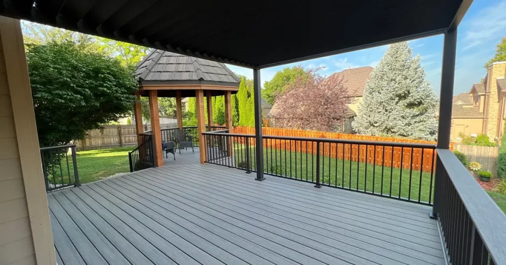 Composite covered deck with black railing and attached gazebo in a landscaped backyard with privacy fence featured