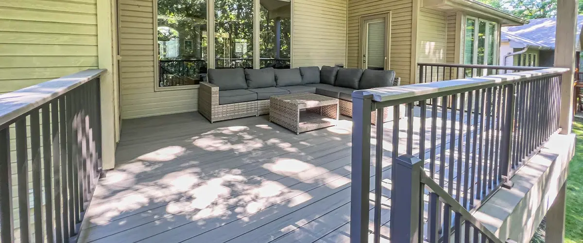 Covered composite deck with outdoor sectional sofa and black metal railing attached to modern house