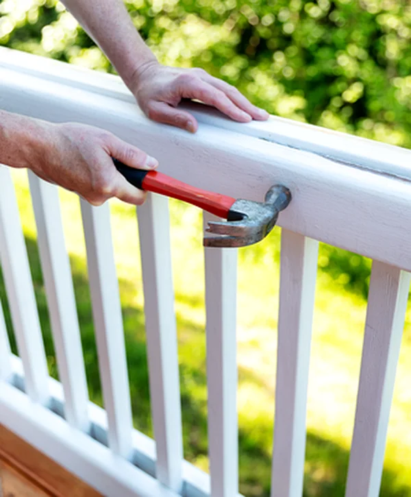 deck installation repair lincoln ne deck building man using claw hammer to repair white wooden deck railing outdoors