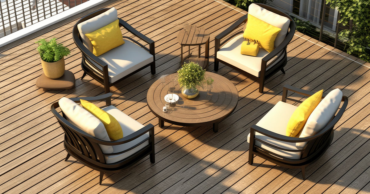 Four modern black-framed patio chairs with cream cushions and bright yellow pillows on a warm brown wooden deck, centered around a round table.
