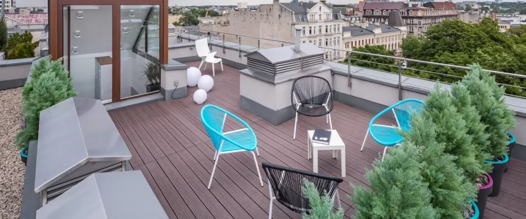 Rooftop deck featuring dark brown flooring, various low-maintenance evergreens in planters, and bright accent furniture including turquoise and black string chairs.