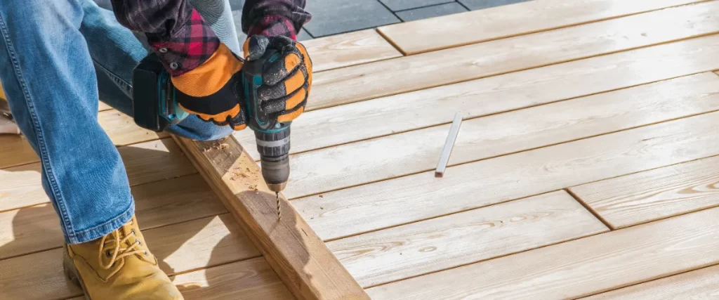 a person using a cordless drill to build an outdoor wooden deck.
