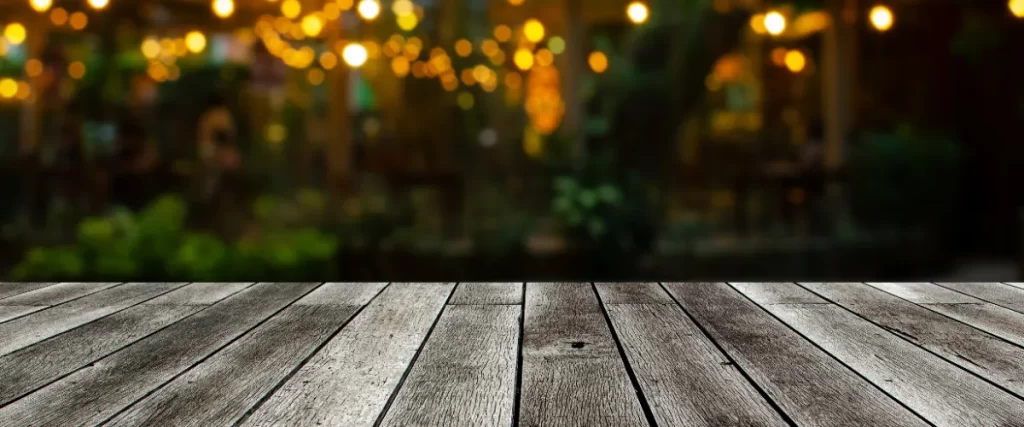 an empty wooden table or terrace with a blurred background of lights from an outdoor evening setting