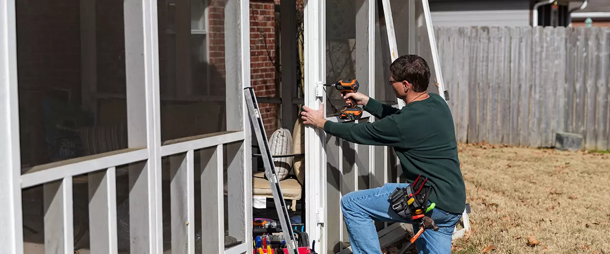 The 5 Best Deck Repair Companies In Lincoln, NE A skilled contractor using a power drill to repair the wooden frame of a screened-in porch or deck door, demonstrating professional deck repair services.