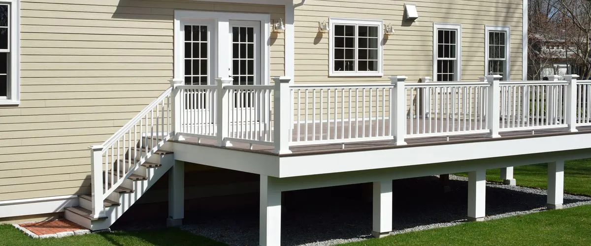 A beautiful elevated backyard deck featuring white vinyl railings, composite decking, and a full staircase leading down to the lawn.