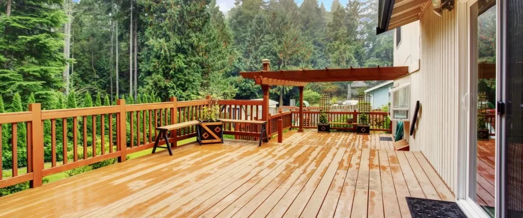 Deck Sealing In Omaha, NE Large wooden deck and pergola showing a rich, protective finish after professional deck sealing, overlooking a lush, wooded backyard.