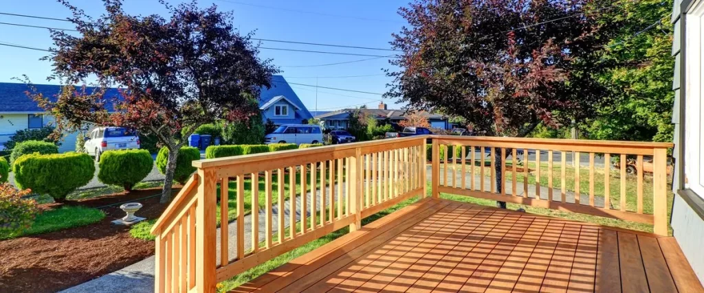 Deck Restoration A newly built or restored wooden deck and railing attached to a house in a suburban setting, featuring steps leading to a well-kept lawn and neighborhood backdrop.