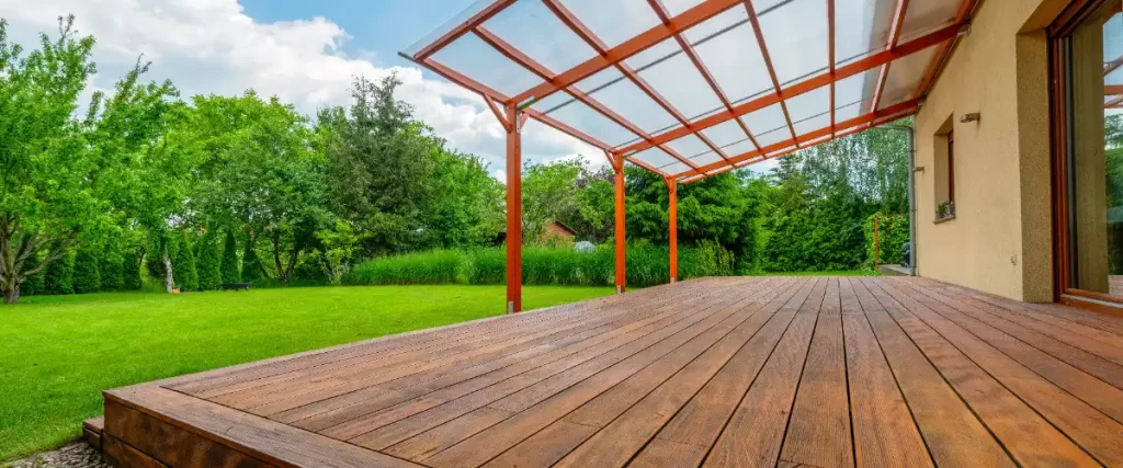 a wooden garden deck with a transparent roof extension, designed to be an outdoor living area connected to a house
