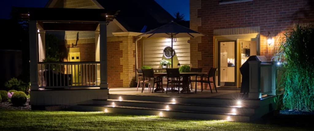 an illuminated outdoor living space featuring a deck, patio furniture, and various types of landscape lighting