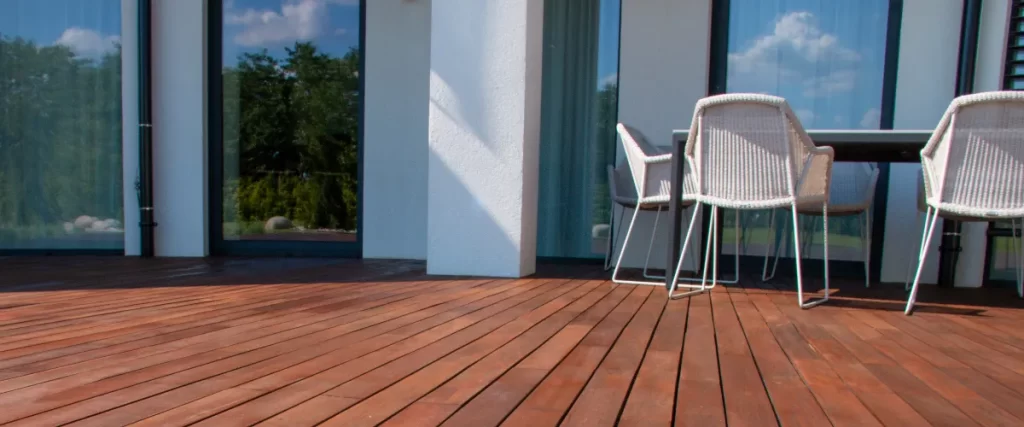 a close-up of a person using a power drill to fasten a wooden deck board with a screw