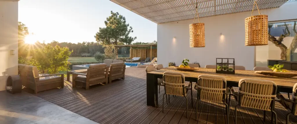 Smart Tech Upgrades for Modern Decks in 2026 (Lighting, Outlets, Sound) a modern patio area with a wooden deck and large sliding glass doors leading into an illuminated interior living space