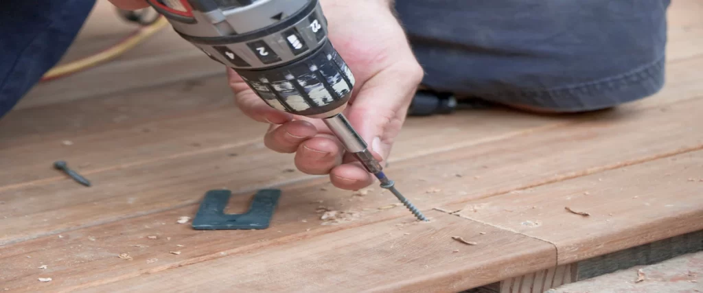 Wind-Resistant Deck Design for the Omaha–Lincoln Corridor A close-up of a power tool being used to secure a fastener into a wooden plank for a new deck roof installation.