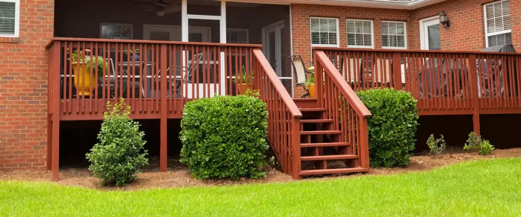 Wind-Resistant Deck Design for the Omaha–Lincoln Corridor An outdoor wooden deck stained in deep redwood with vertical slat railings and a short staircase leading to a green lawn.