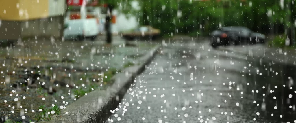 Protecting Your Deck From Hail in Eastern Nebraska Heavy hail stones falling on a wet Nebraska street with blurred cars and green trees in the background.