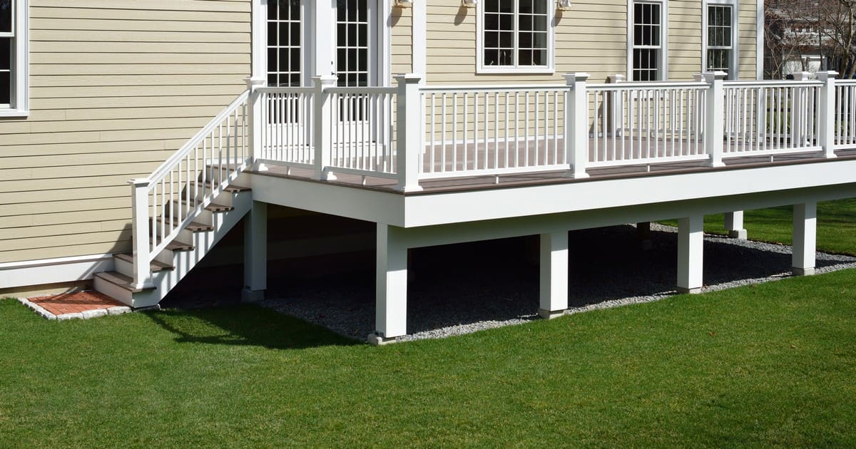 A large, elevated custom backyard deck featuring a wind-resistant deck design with white classic railings and integrated stairs.