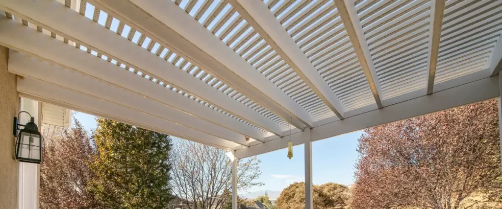 Wind-Resistant Deck Design for the Omaha–Lincoln Corridor A view looking up at a white slatted deck roof or pergola providing shade over an outdoor living space during a clear day.