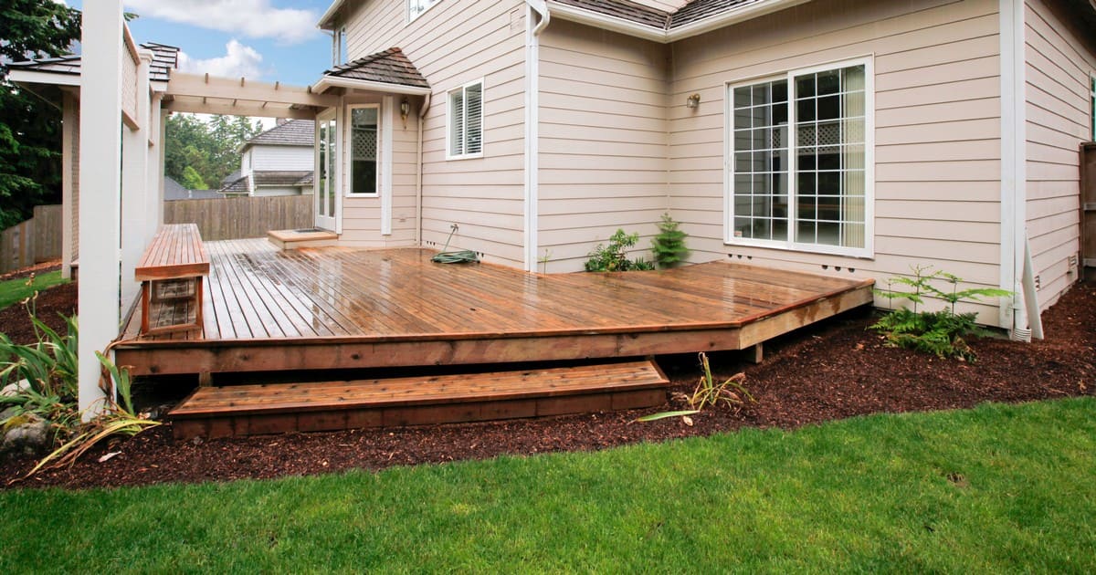 A freshly stained wooden deck design for a pole barn home in Nebraska featuring a built-in bench and a small decorative pergola structure.