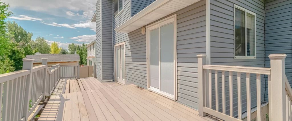 Deck Design for Pole Barn Homes & Shouses in Nebraska Large, sprawling light-grey wooden deck with white safety railings and multiple sliding door access points on a modern residential home.