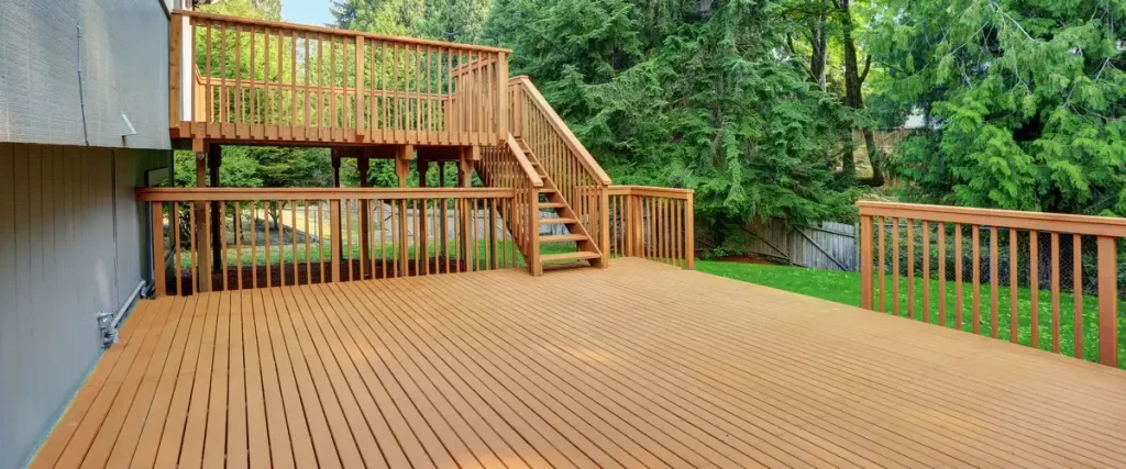 An expansive two-story wooden deck featuring a multi-level design, connecting stairs, and a secure railing system overlooking a lush green backyard.