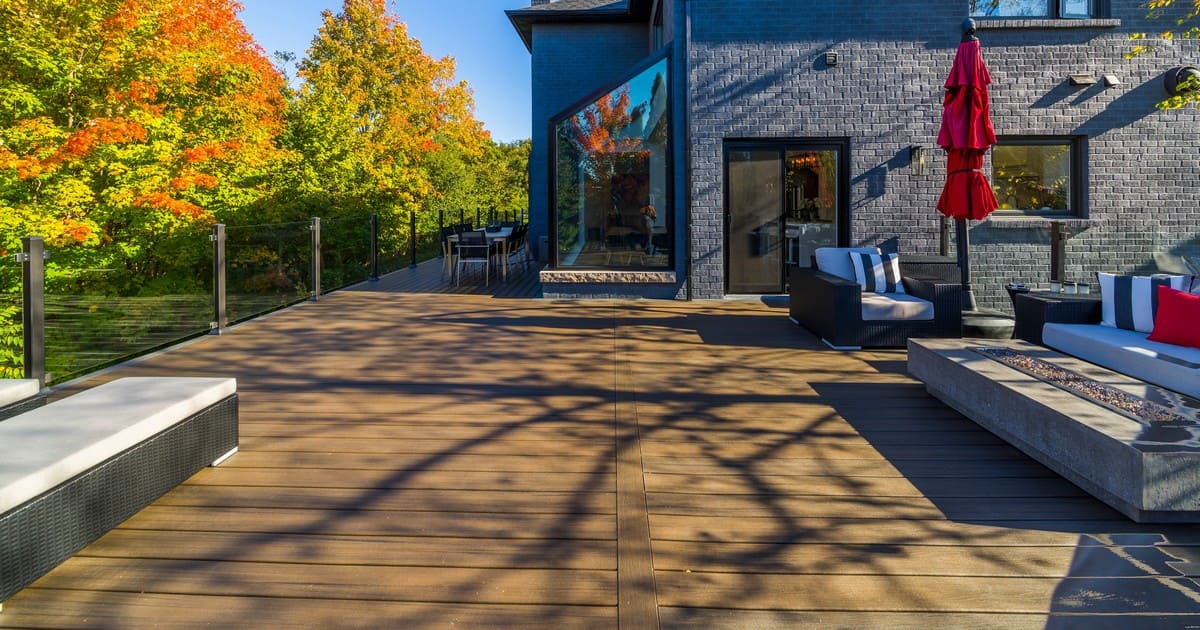 A modern, high-end composite deck addition featuring a fire pit table, lounge furniture, and glass railings, designed for homes with septic systems.