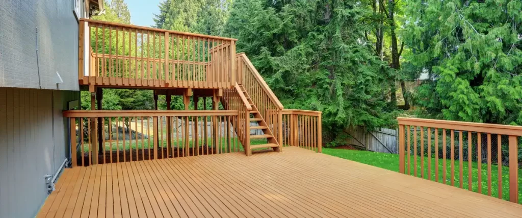 Deck Design for Pole Barn Homes & Shouses in Nebraska High-elevation multi-level wooden deck with tall support posts and connecting stairs overlooking a dense green forest backyard.