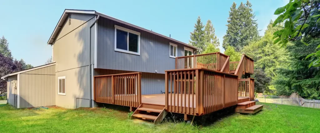 Deck Design for Pole Barn Homes & Shouses in Nebraska Full exterior view of a grey two-story house featuring a large multi-level red-stained wood deck with stairs and a spacious lawn.