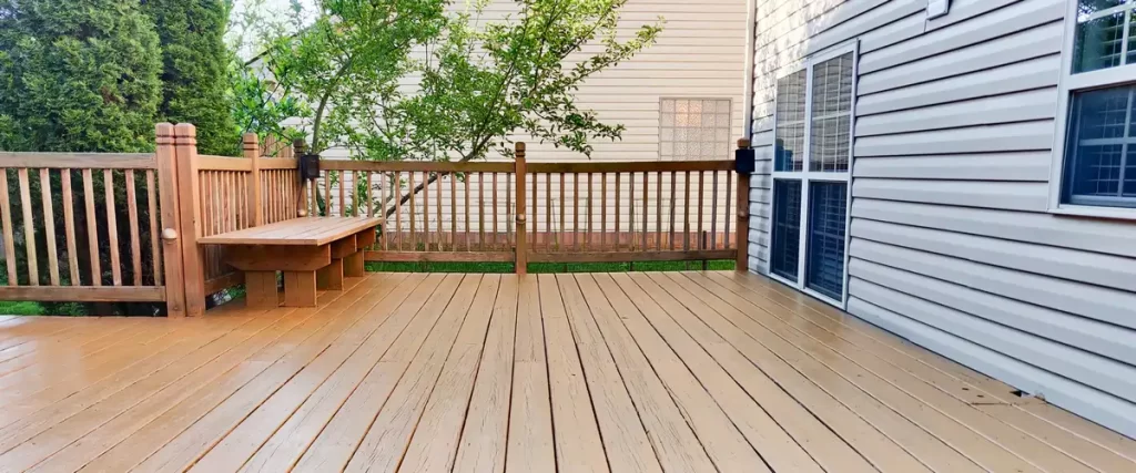 Deck Design for Pole Barn Homes & Shouses in Nebraska Close-up of a light-stained wooden deck featuring an integrated bench seat and railing next to a sliding glass door.