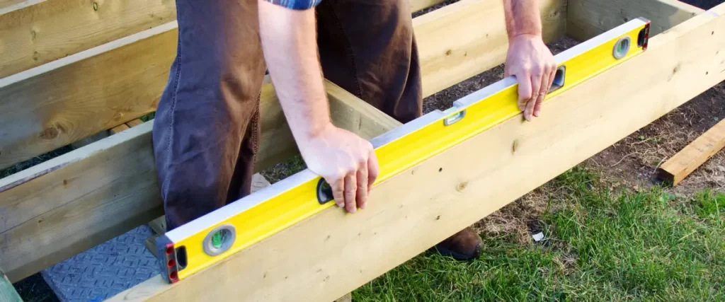 Builder carrying out a deck inspection by placing a large yellow spirit level across the newly installed wooden floor joists.