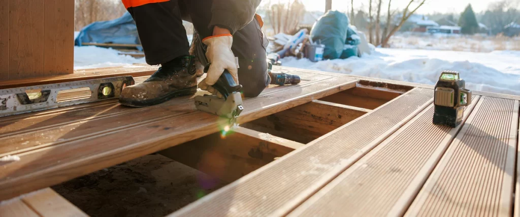 Deck Installation In North Bend, NE builder-installing-deck-boards-with-fasteners-in-winter-snow.webp