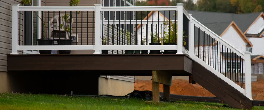 A completed dark brown composite deck featuring elegant white deck railings with black metal balusters and potted plants.