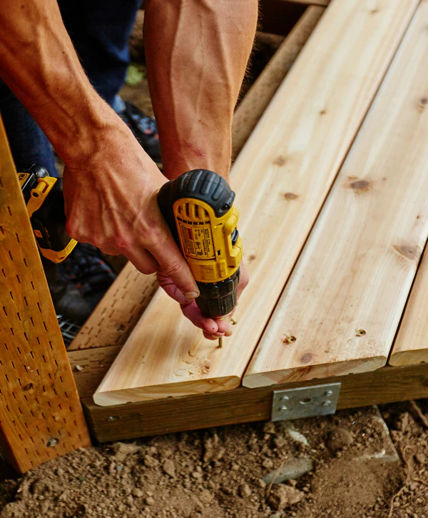 Close-up of a contractor from top deck repair companies in Arlington, TN using a yellow power drill to fasten new wooden boards during a deck restoration project.