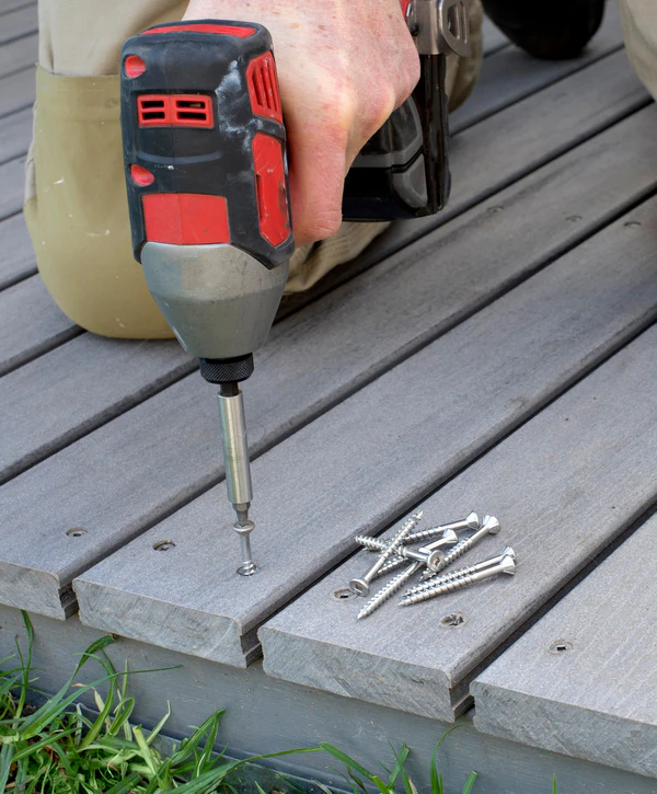 A contractor using a power drill to fasten screws into gray composite decking boards during a deck repair project in Underwood, IA.
