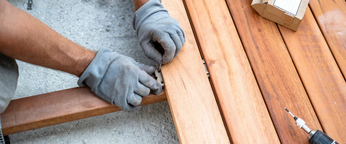 Gloved hands carefully placing a hidden fastener clip between wooden boards during a deck repair and installation project.
