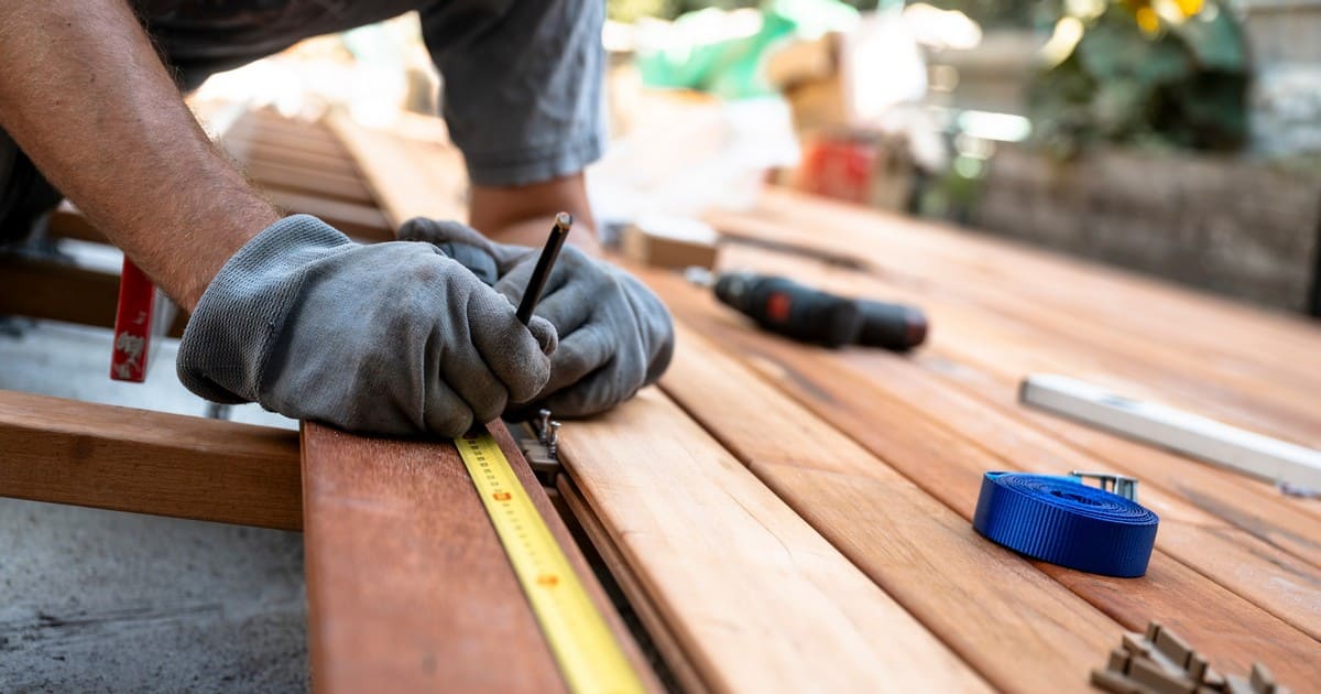 Contractor conducting a thorough deck inspection Omaha by measuring and marking wooden deck boards with a pencil and tape measure.