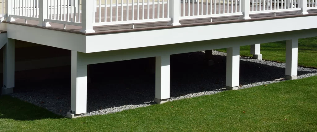 White structural support posts safely secured to concrete deck footings, resting in a bed of decorative gravel beneath a low-profile deck.
