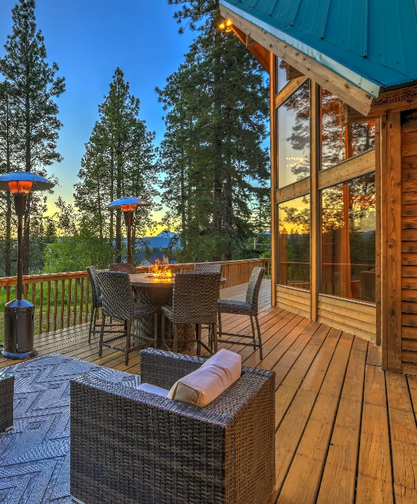 An inviting wooden deck at sunset attached to a cabin-style home, furnished with a glowing fire pit table, wicker chairs, and patio heaters, highlighting premium deck building in Chalco, NE.