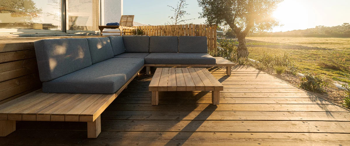 A beautiful finished wooden deck featuring a modern gray sectional sofa and coffee table, showcasing the results of expert deck maintenance.
