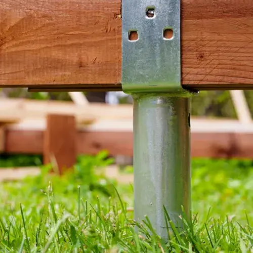 A close-up view of a galvanized steel post base connector supporting a heavy timber beam for a sturdy deck foundation.